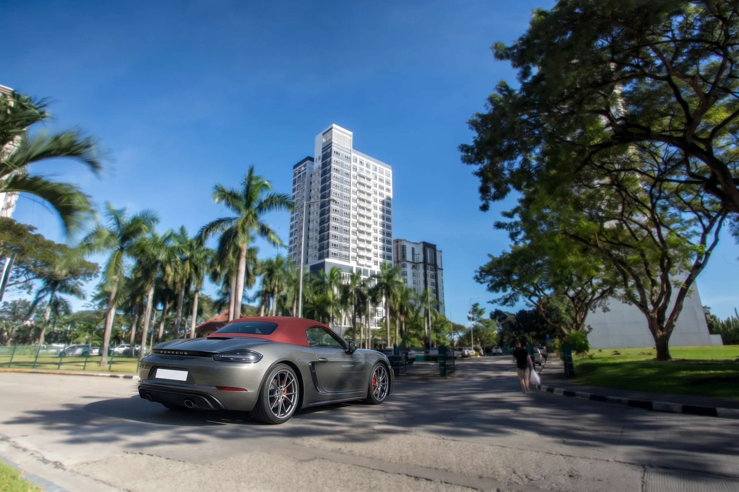 An Agate Grey Porsche 718 Boxster with a red soft top on a palm-lined city street