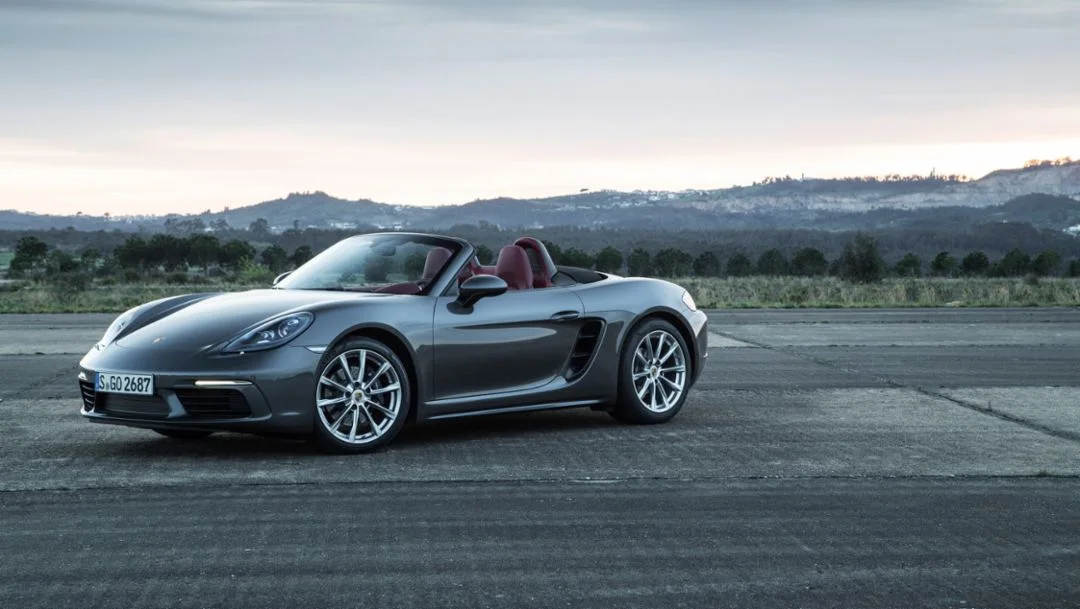 Agate Grey Porsche 718 Boxster with its roof down, photographed from the front and side